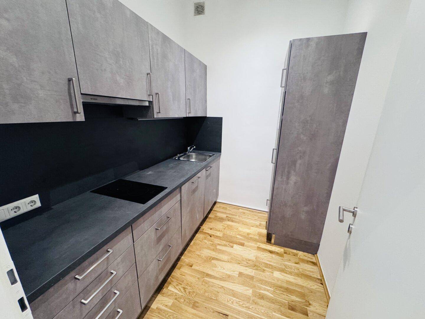 Moderne Küchenzeile mit grauen Schränken, Induktionskochfeld und Dunstabzugshaube.