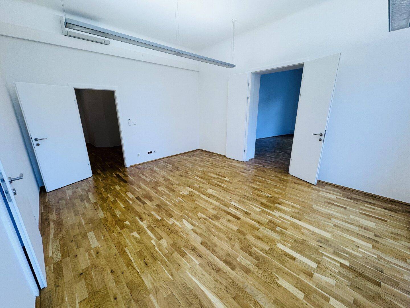 Großer Büroraum mit Holzboden und mehreren Türen, die zu anderen Bereichen führen.