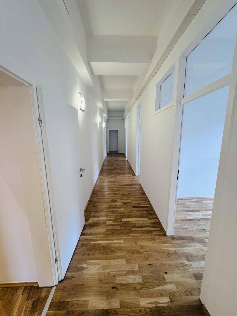 Langer, heller Flur mit Holzboden und mehreren Türen, der die verschiedenen Büros verbindet.