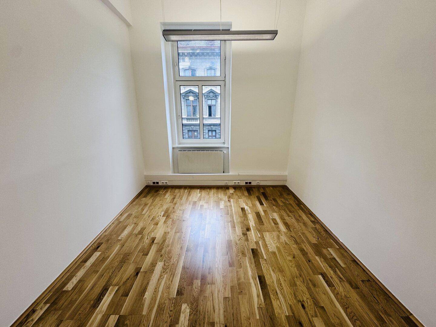 Kleiner Büroraum mit Holzboden und einem Fenster, das auf die Straße blickt.