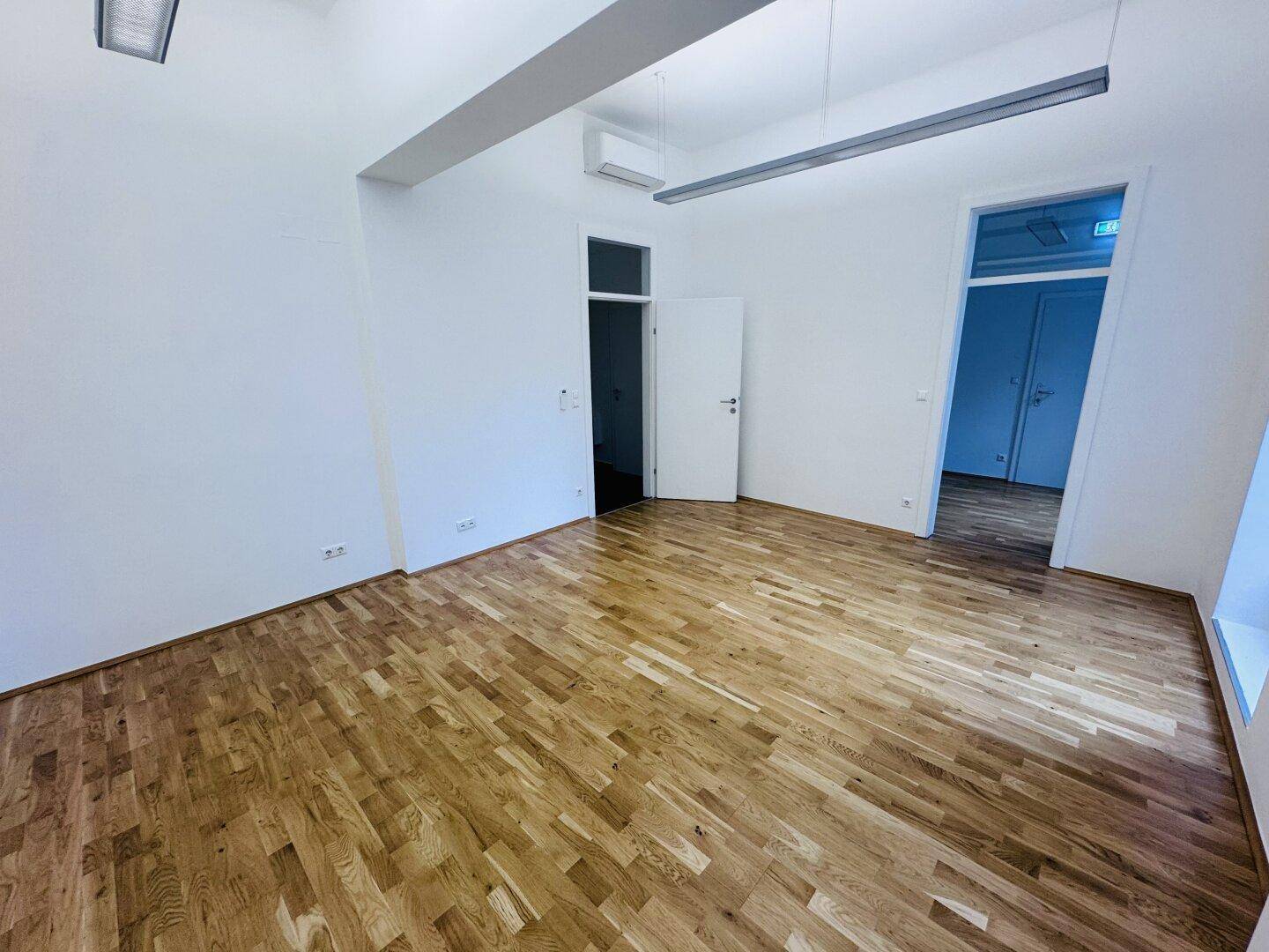 Geräumiger Büroraum mit Holzboden, Klimaanlage und Zugang zu weiteren Räumen.