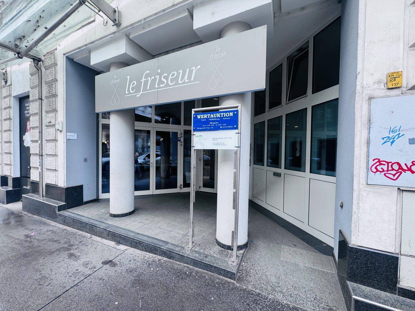 Gebäudefassade mit einem Friseursalon-Schild und einem Aushang für eine Wertauktion.