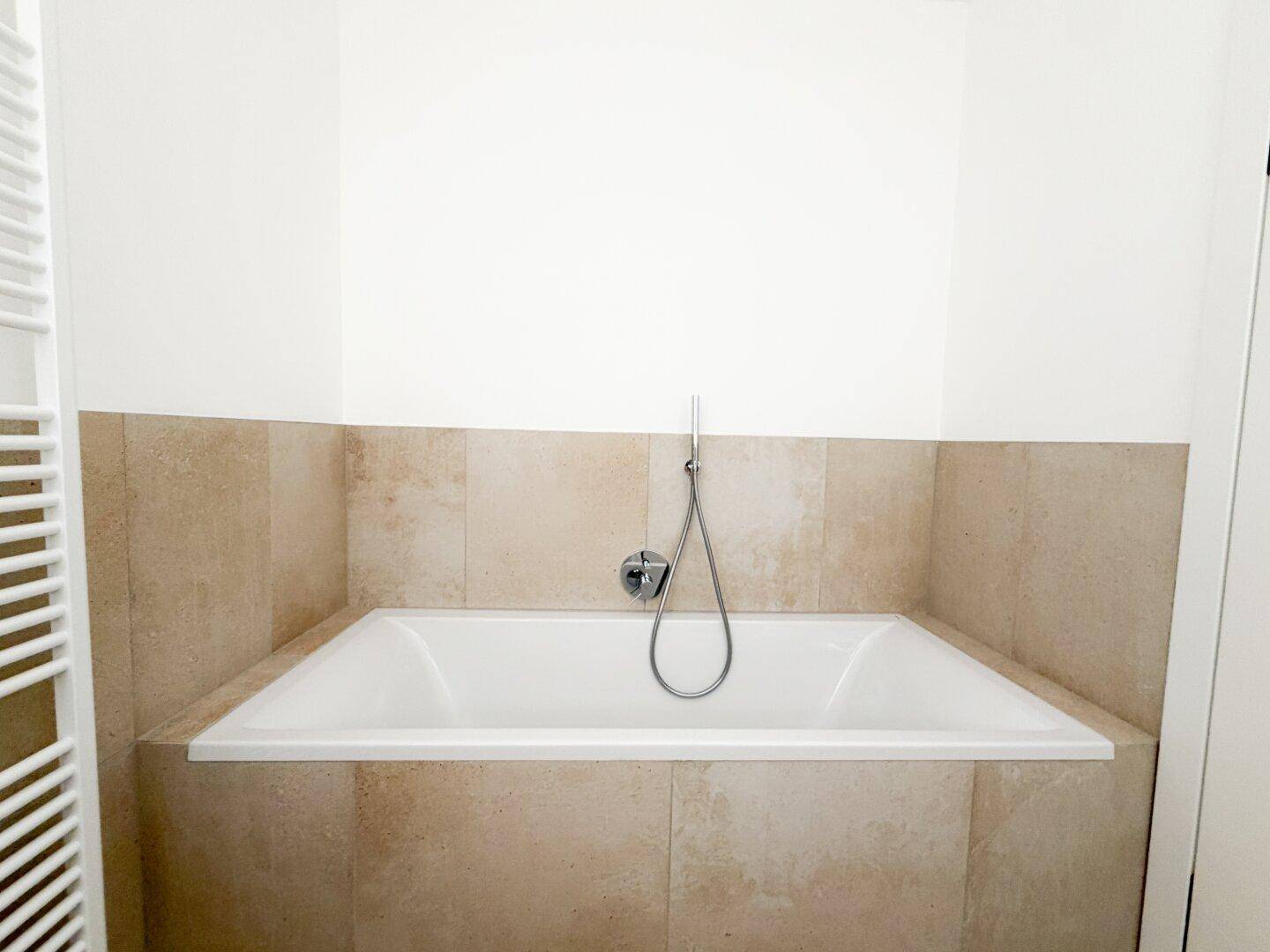 Eingebaute Badewanne in einem modernen Badezimmer mit beigefarbenen Fliesen.