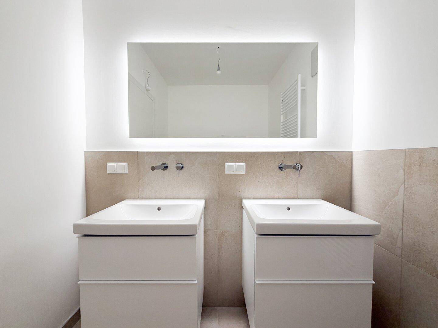 Modernes Badezimmer mit zwei Waschbecken und einem großen, beleuchteten Spiegel.