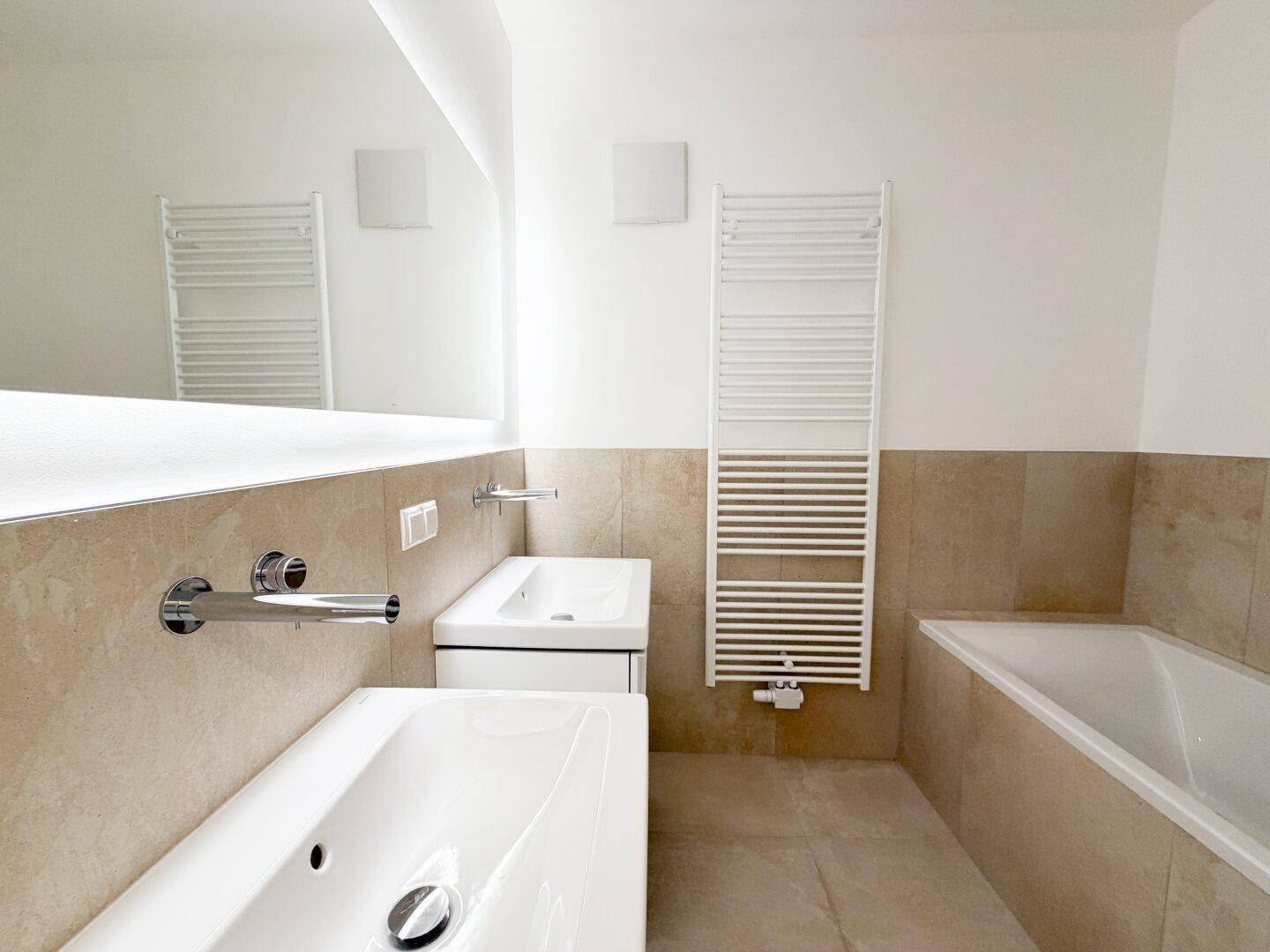 Modernes Badezimmer mit zwei Waschbecken, Badewanne und einem beheizten Handtuchhalter.