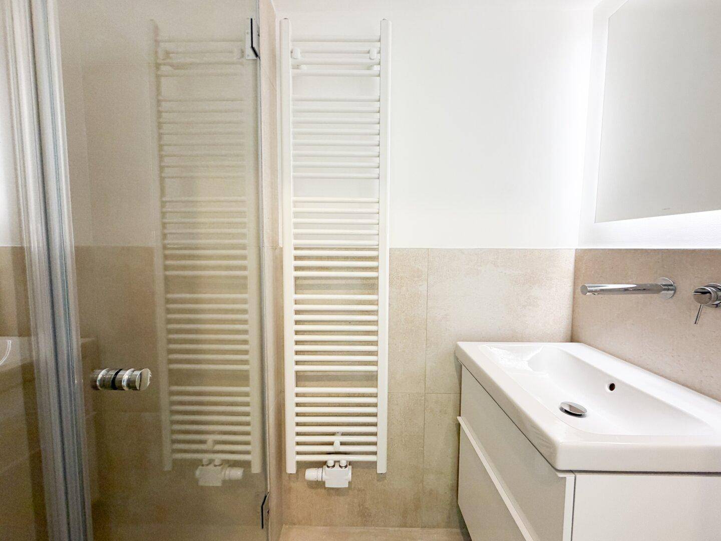 Modernes Badezimmer mit Waschbecken, beheiztem Handtuchhalter und Duschabtrennung aus Glas.