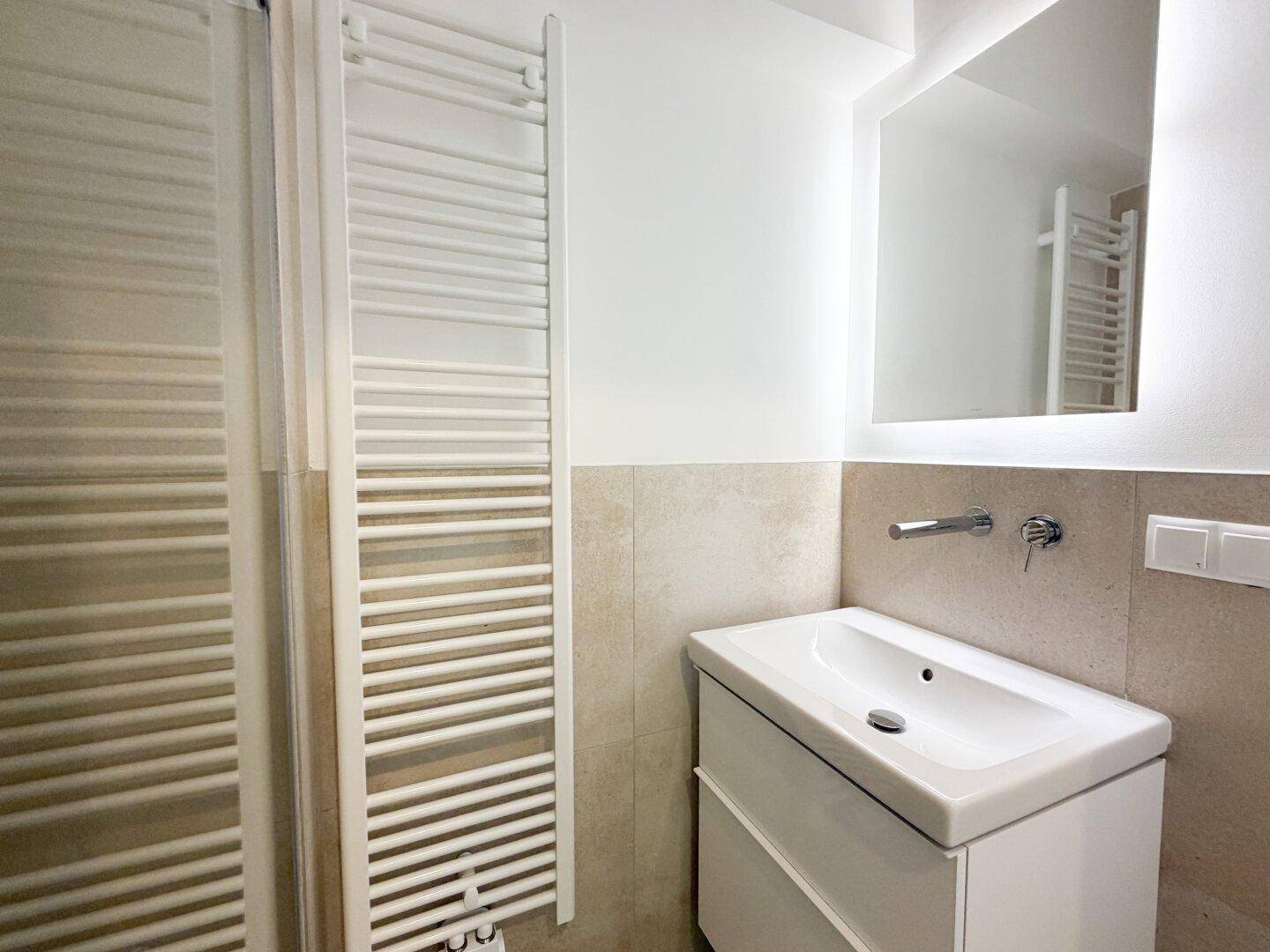 Modernes Badezimmer mit Waschbecken, beheiztem Handtuchhalter und beleuchtetem Spiegel.