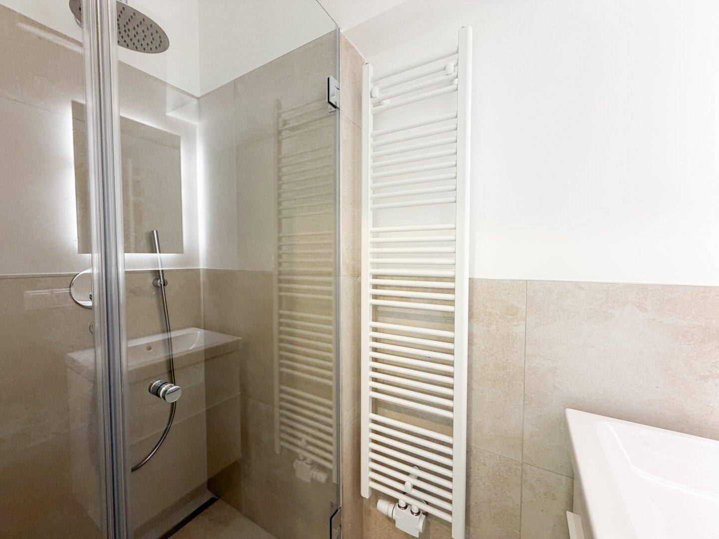 Modernes Badezimmer mit ebenerdiger Dusche, beheiztem Handtuchhalter und beigefarbenen Fliesen.
