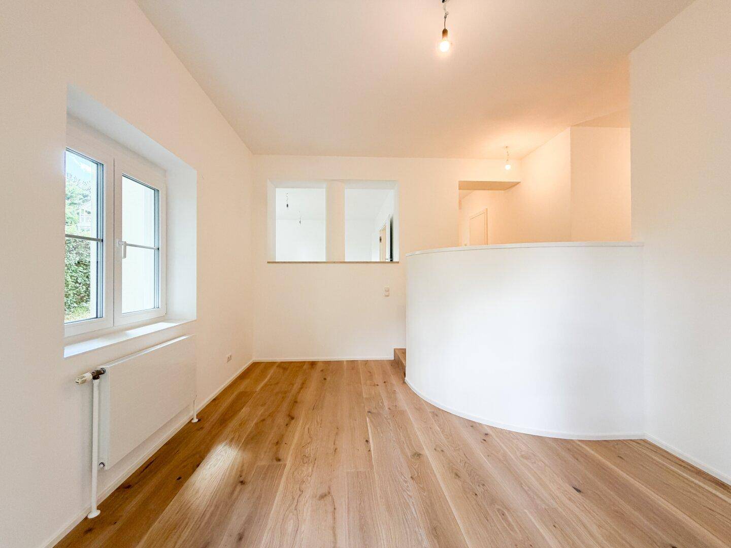 Heller Raum mit Holzfußboden, Fenster und einer modernen, geschwungenen Trennwand.