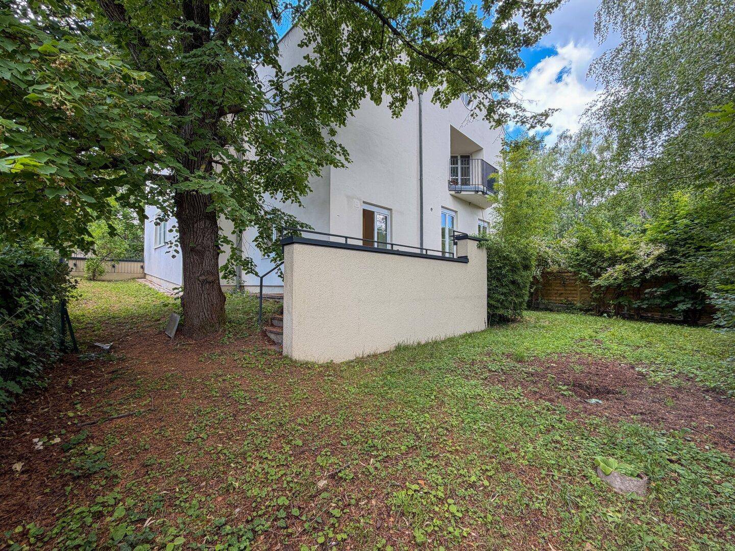 Weitläufiger Garten mit altem Baumbestand und Blick auf die Gebäudefassade mit Balkon.