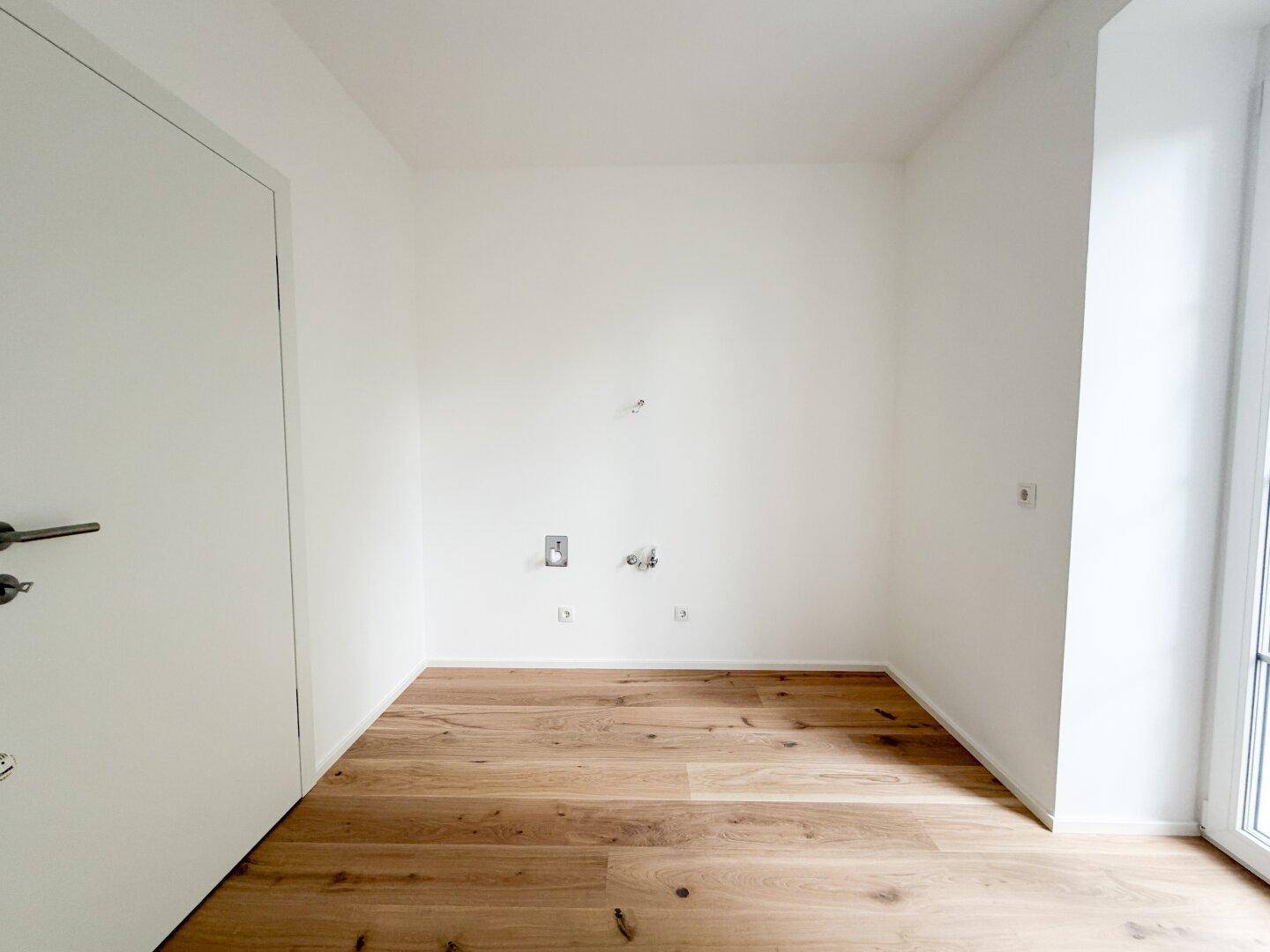 Heller Raum mit Holzfußboden, französischen Balkontüren und sichtbaren Anschlüssen für Installationen.
