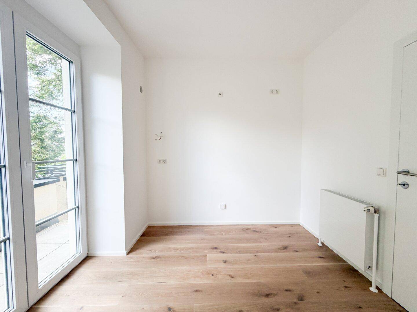 Heller Raum mit Holzfußboden, Heizkörper und Zugang zu einem französischen Balkon.