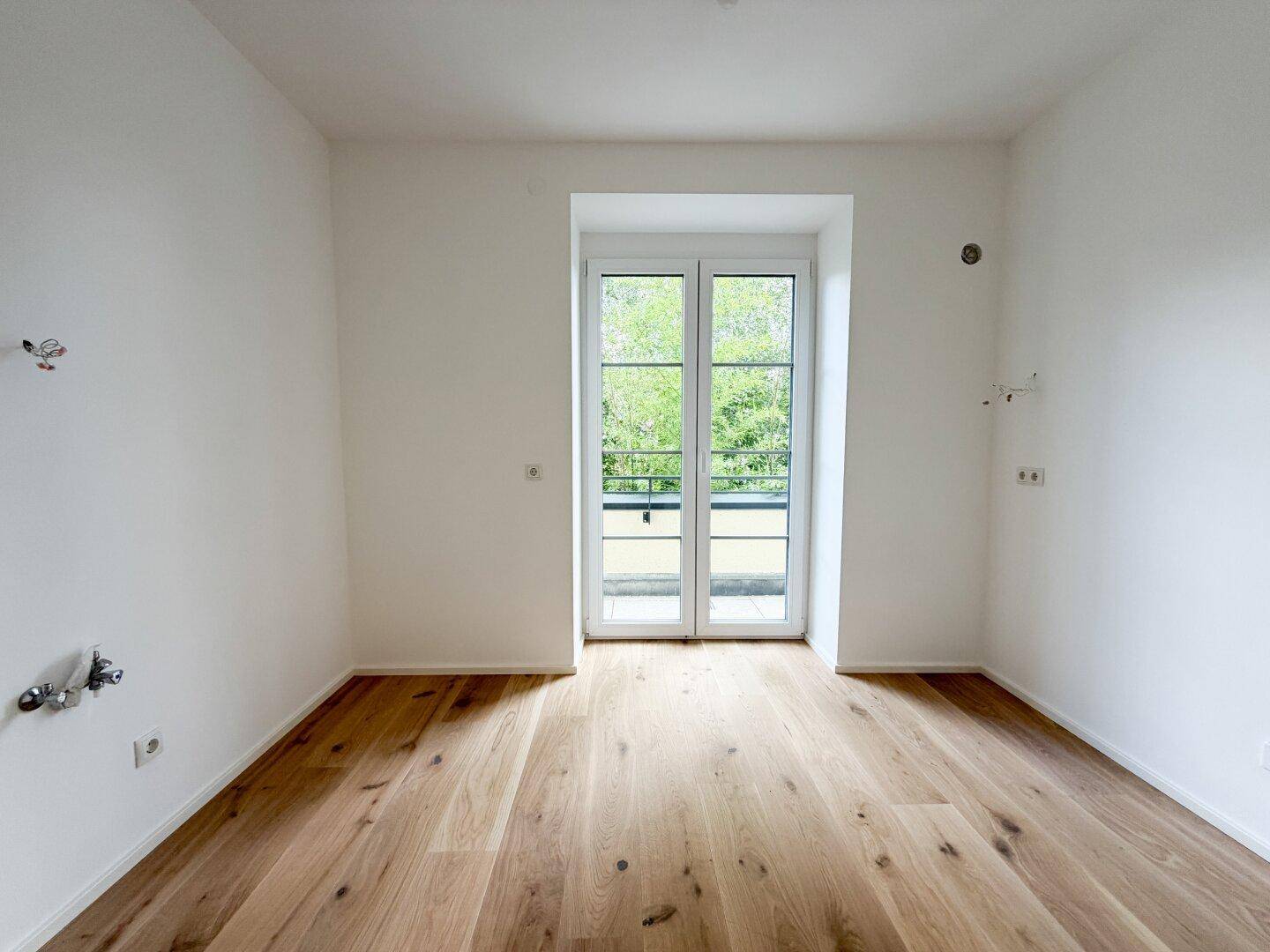 Heller Raum mit Holzfußboden und französischen Balkontüren, vorbereitet für weitere Installationen.