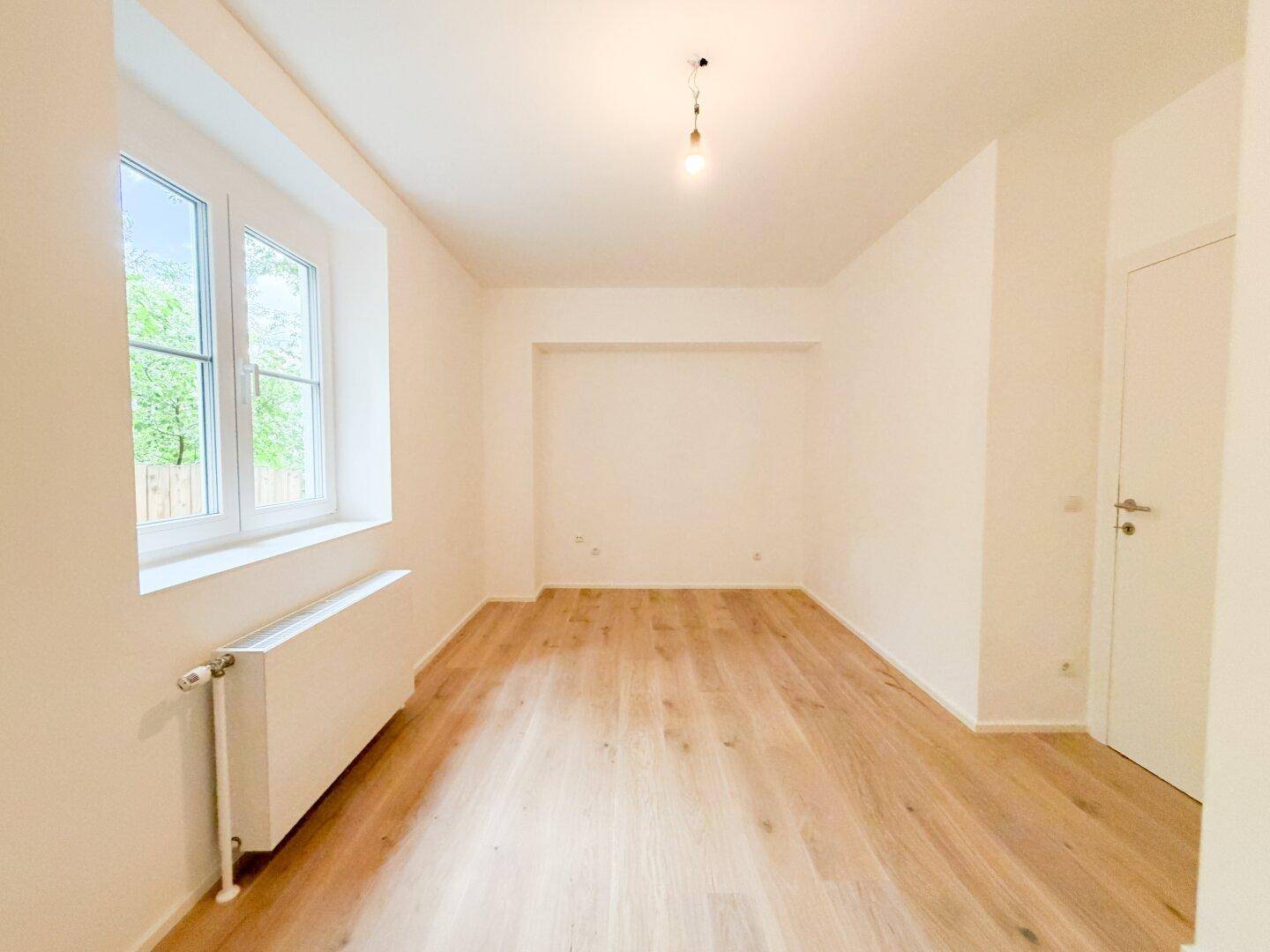 Heller Raum mit Holzfußboden, Fenster und einer praktischen Nische in der Wand.