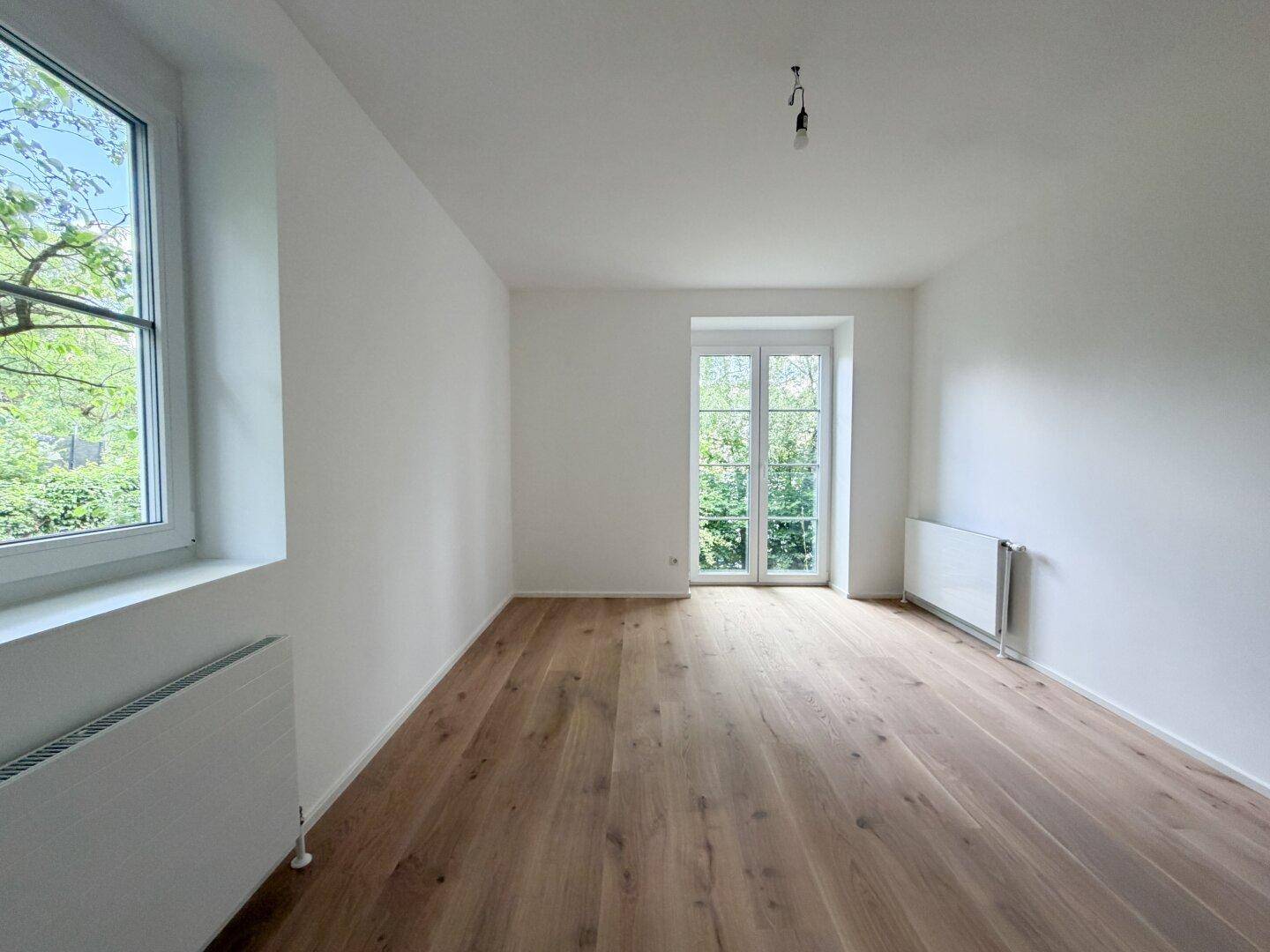 Geräumiger, heller Raum mit Holzfußboden, Fenster und französischen Balkontüren.