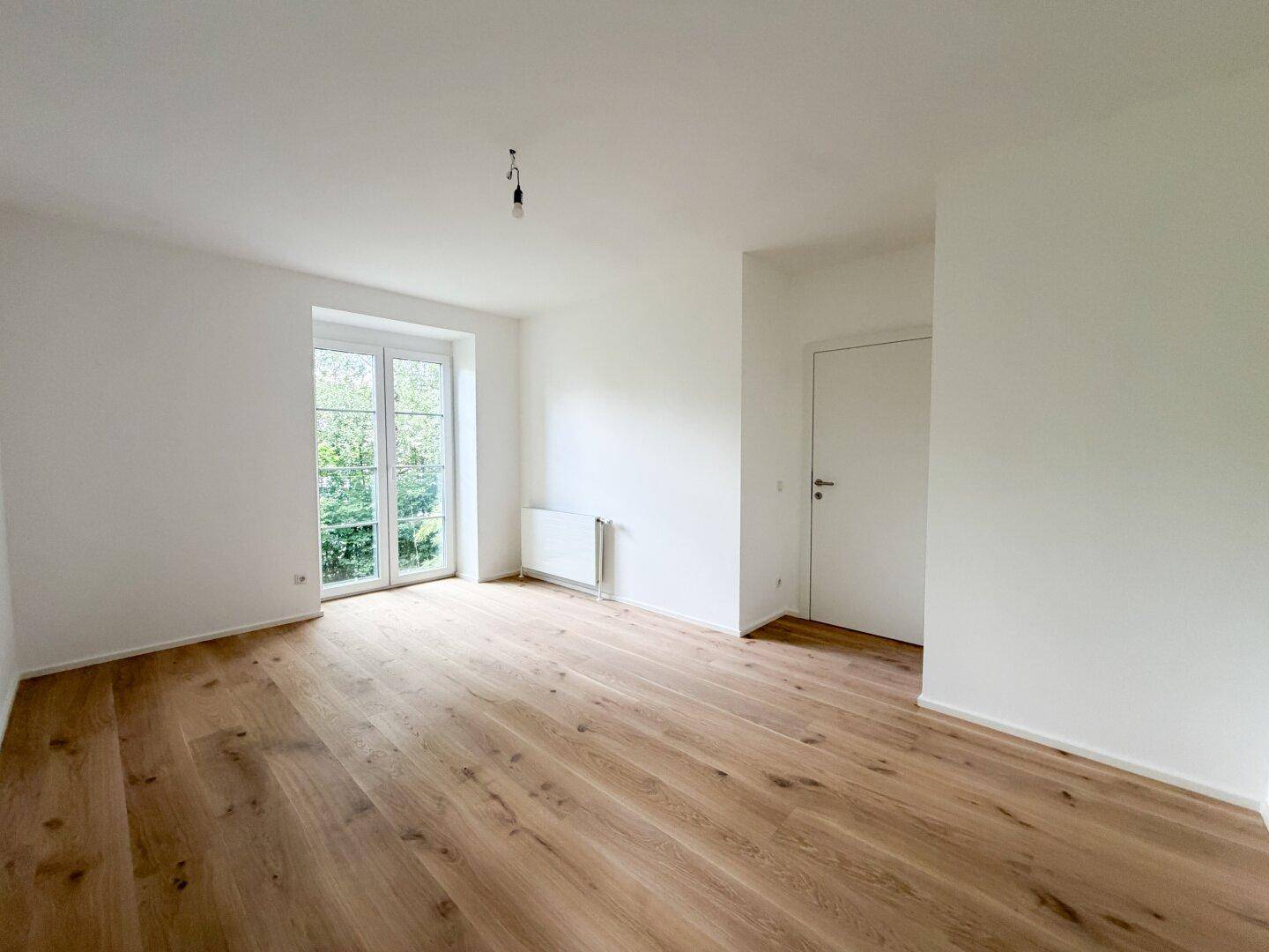 Heller Raum mit Holzfußboden, französischen Balkontüren und einer weiteren Tür.