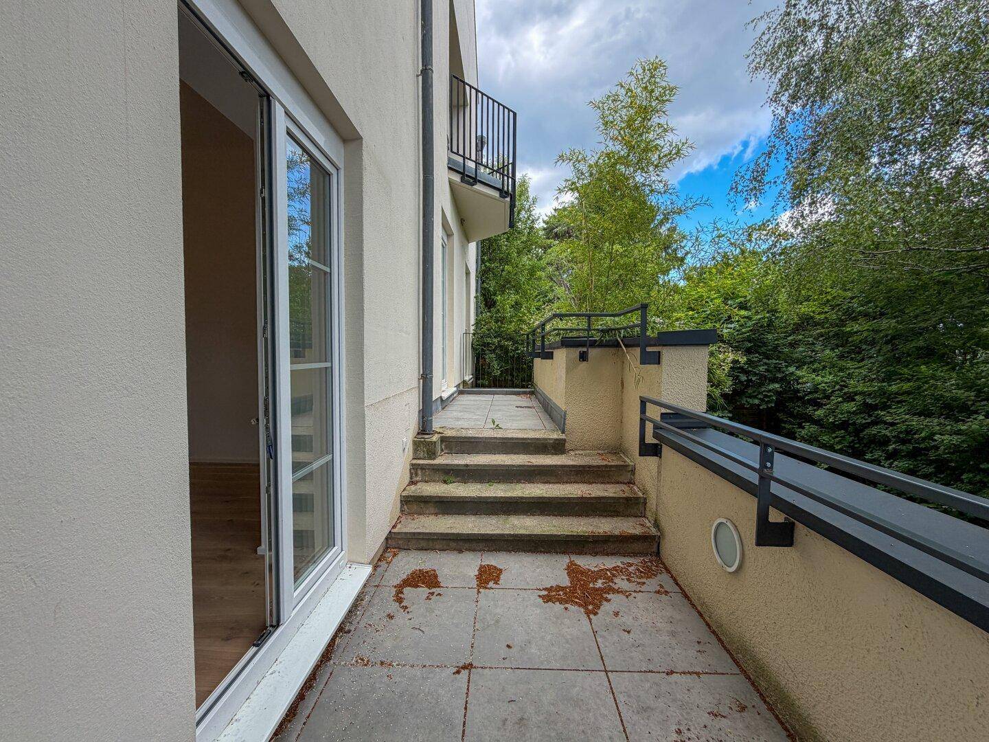 Geräumige Terrasse mit Treppenaufgang und Blick auf die umliegende grüne Landschaft.