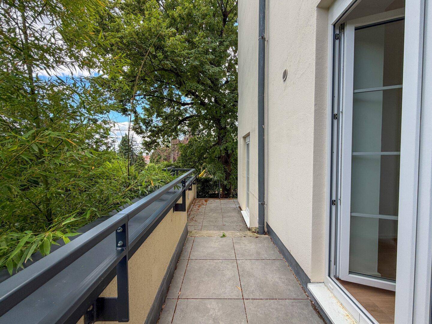 Langer Balkon mit Fliesenboden und Blick ins Grüne, zugänglich vom Innenbereich.