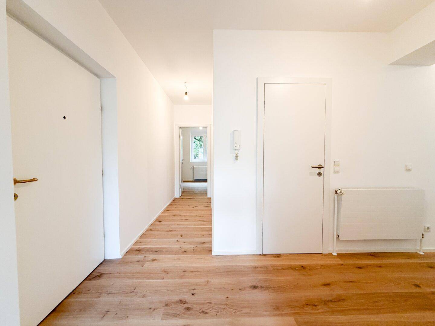 Heller Flur mit Holzboden und weißen Türen, der zu weiteren Räumen führt.
