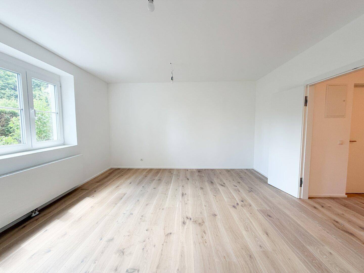 Geräumiger, heller Raum mit neuem Holzfußboden und einem Fenster, das viel Tageslicht hereinlässt.