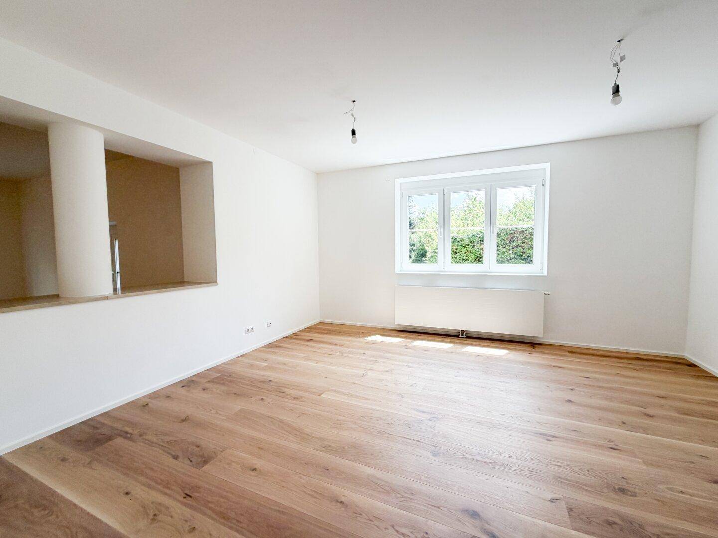 Geräumiger, heller Raum mit neuem Holzfußboden und Blick ins Grüne durch das Fenster.