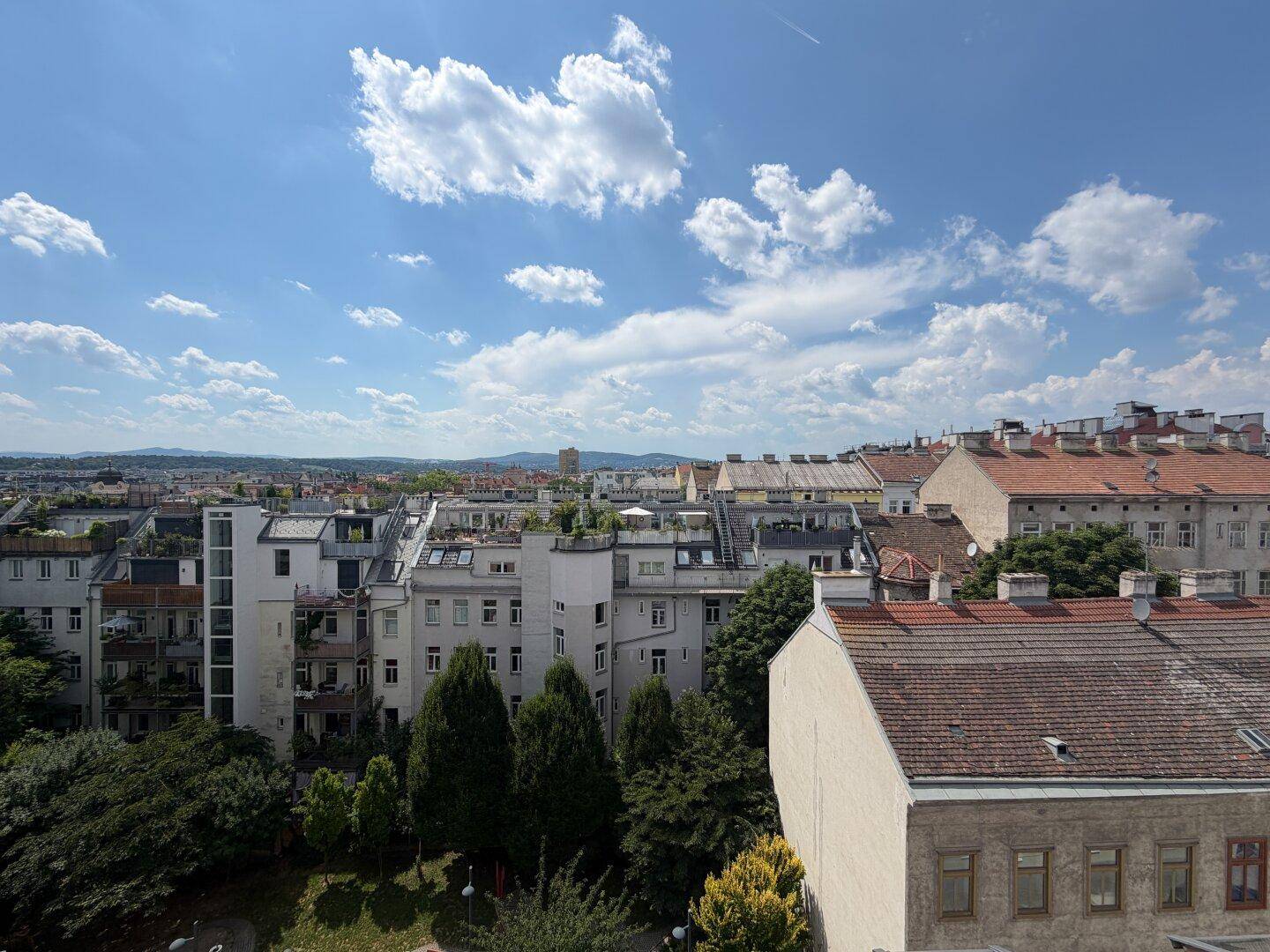 Panoramablick über die Dächer der Stadt mit grünen Bäumen und Bergen am Horizont.