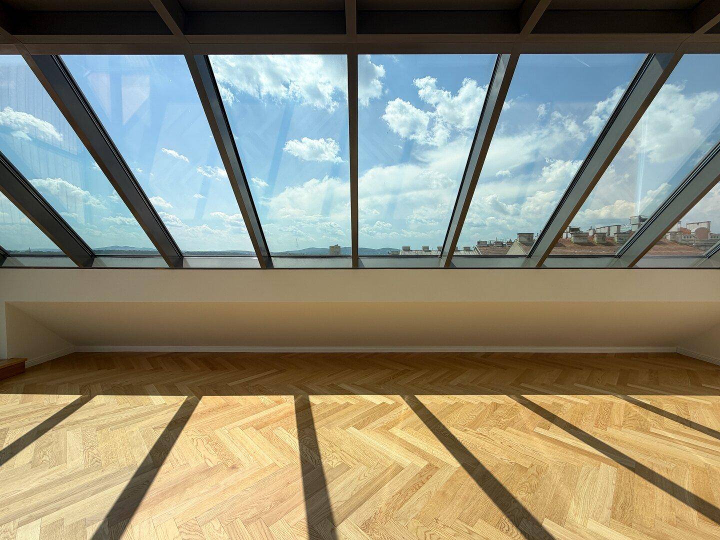 Großzügige Glasfront im Dachgeschoss mit weitem Himmelblick und sonnigem Fischgrätparkett.
