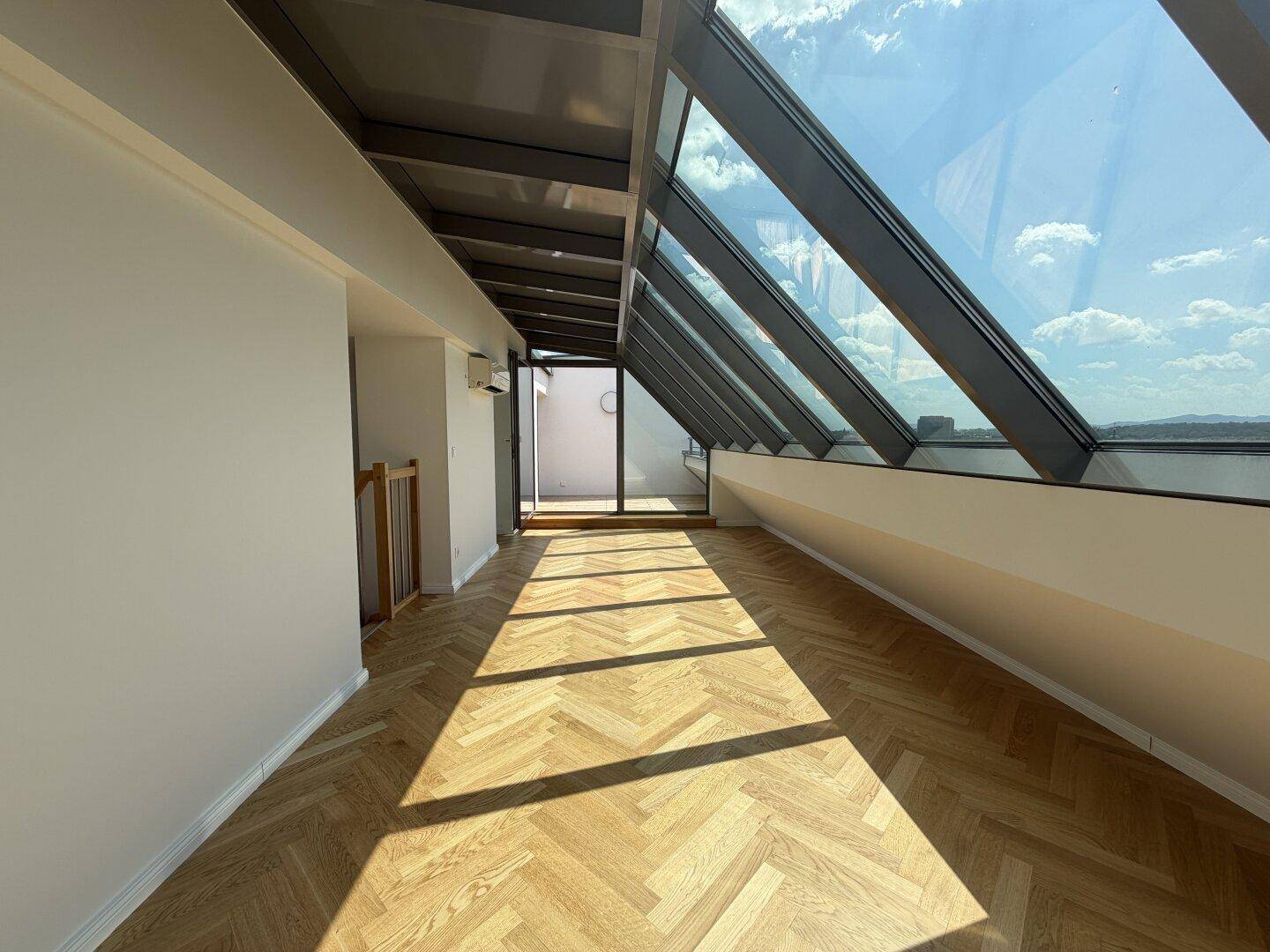 Lichtdurchfluteter Dachraum mit elegantem Fischgrätparkett und beeindruckender Glasfront.