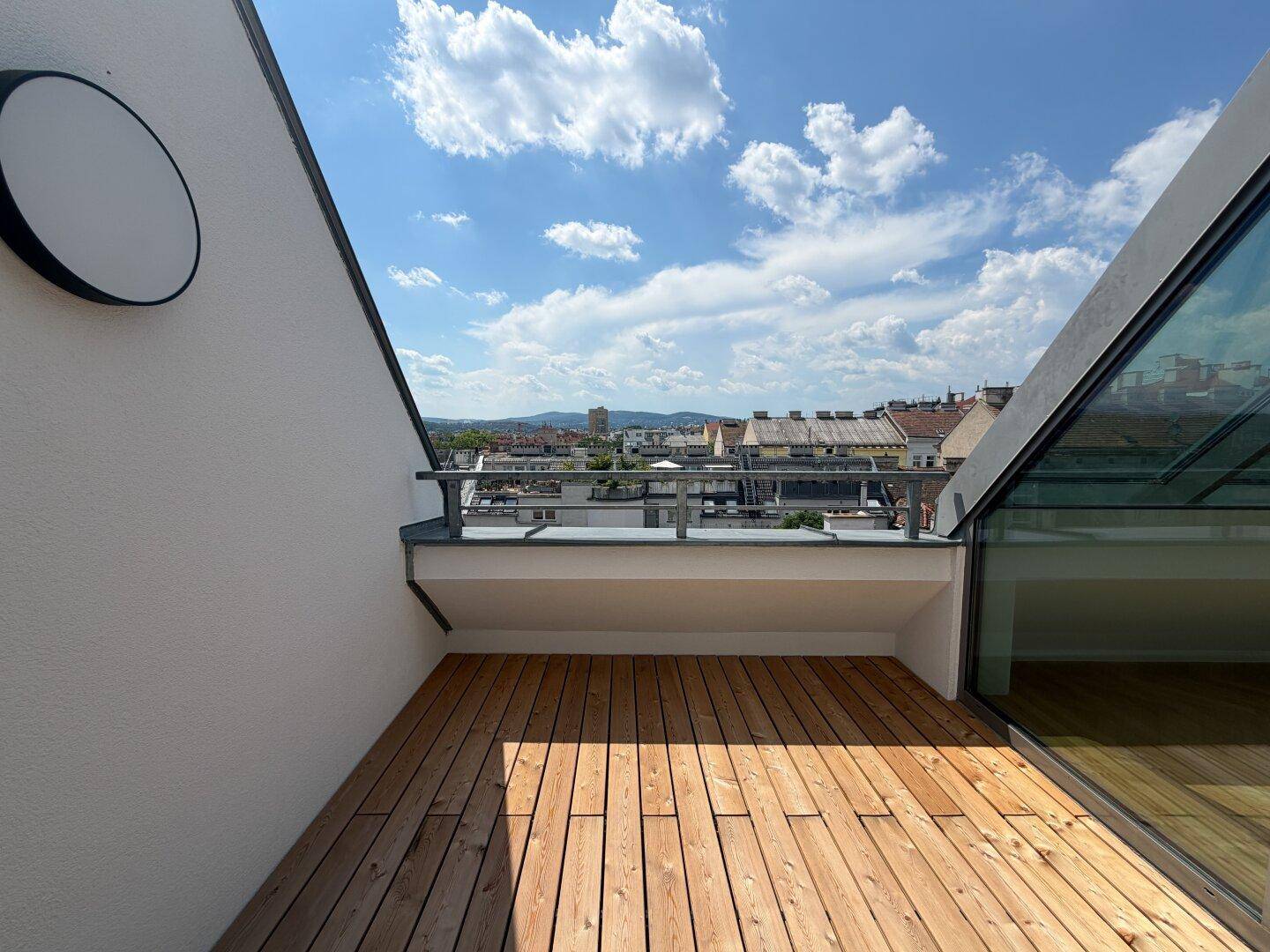 Sonniger Terrassenbereich mit Holzboden und moderner Wandleuchte, bietet Stadtblick.