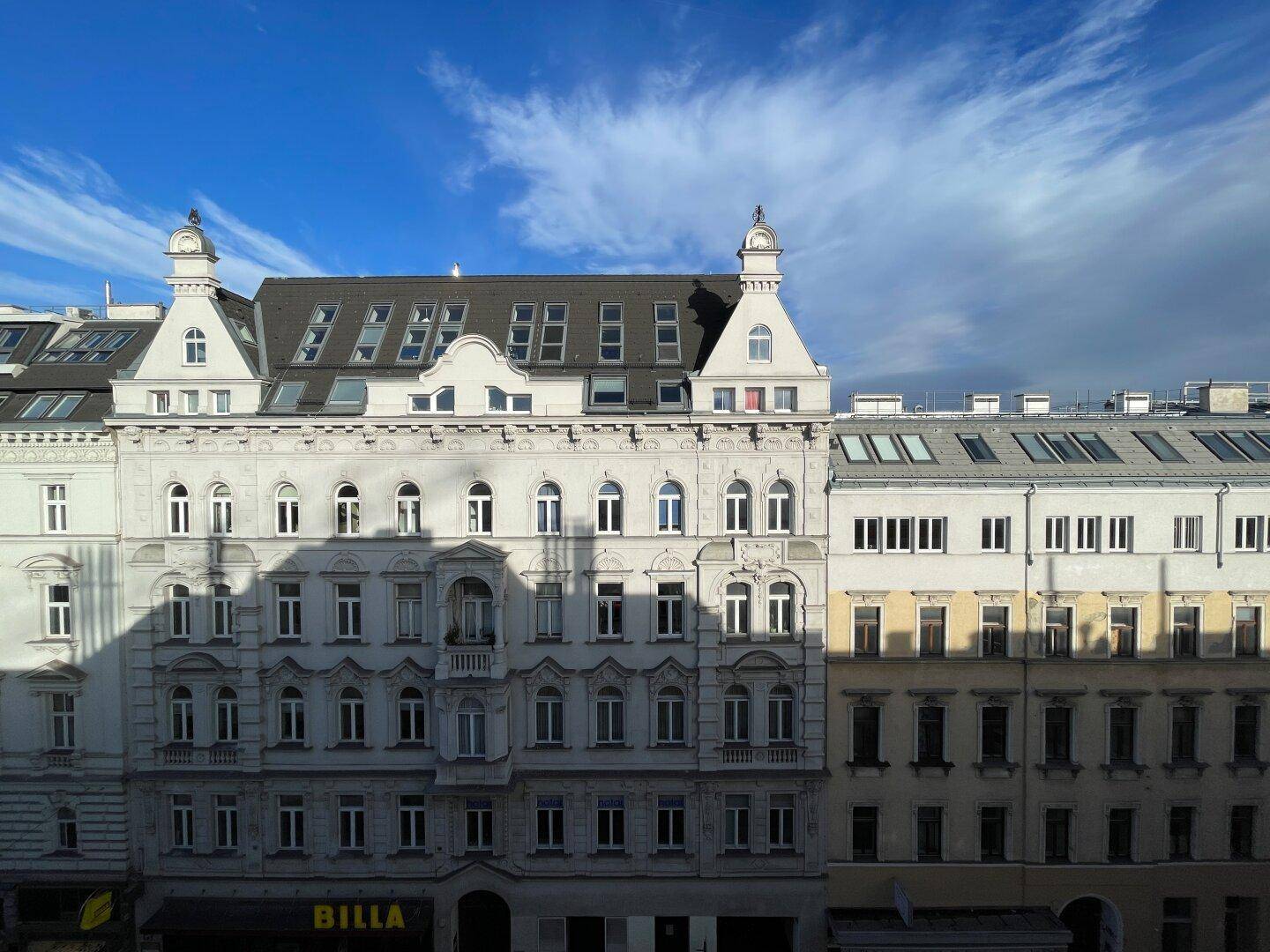 Historische Gebäude mit detailreichen Fassaden und modernen Dachausbauten in städtischer Umgebung.