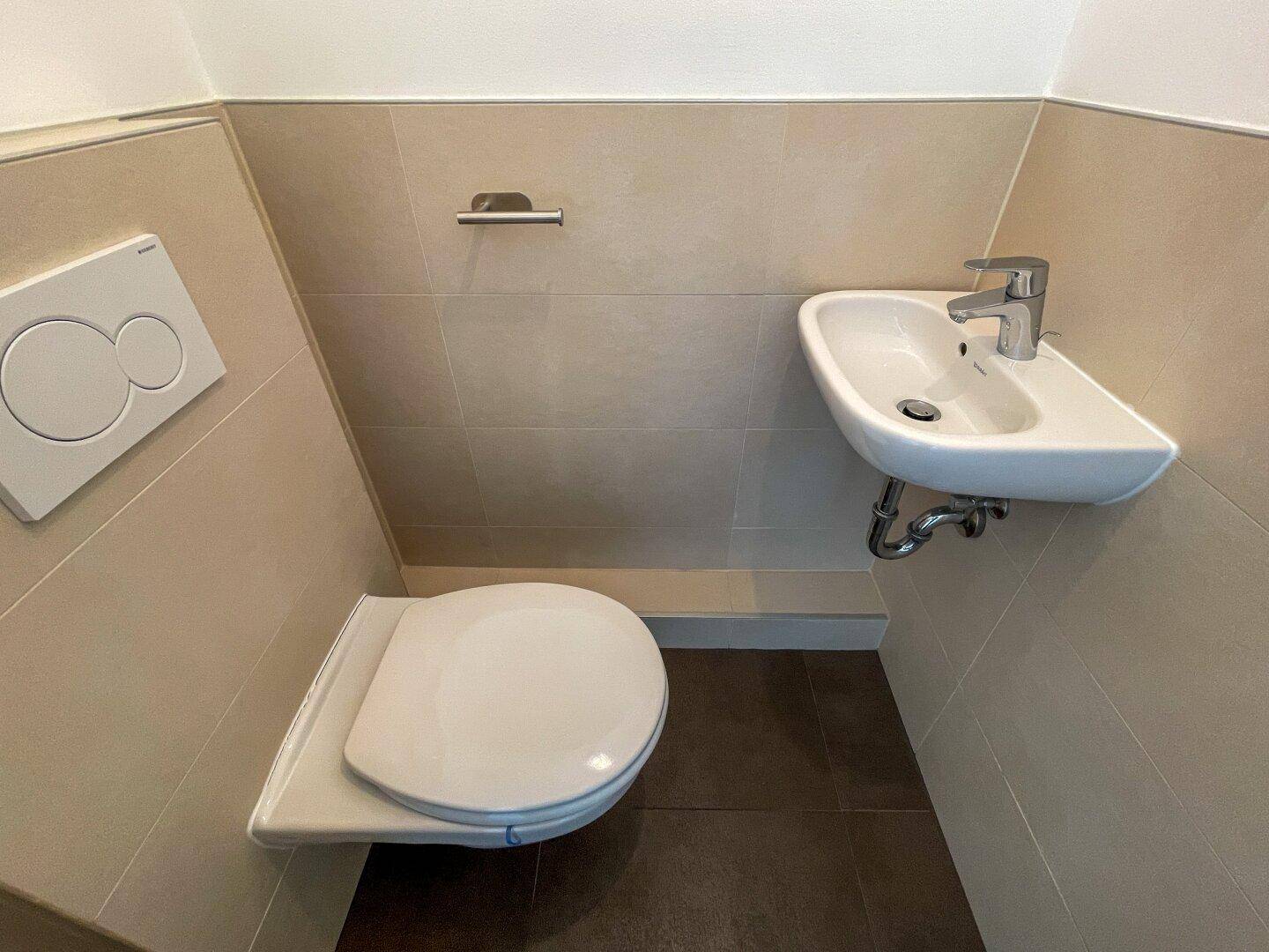 Modernes Gäste-WC mit wandhängendem WC, kleinem Waschbecken und beigefarbenen Fliesen.