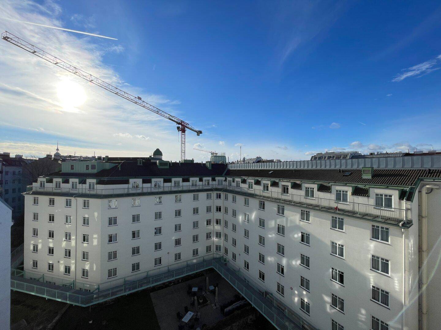 Blick auf ein großes weißes Gebäude mit vielen Fenstern und einem Innenhof unter blauem Himmel.