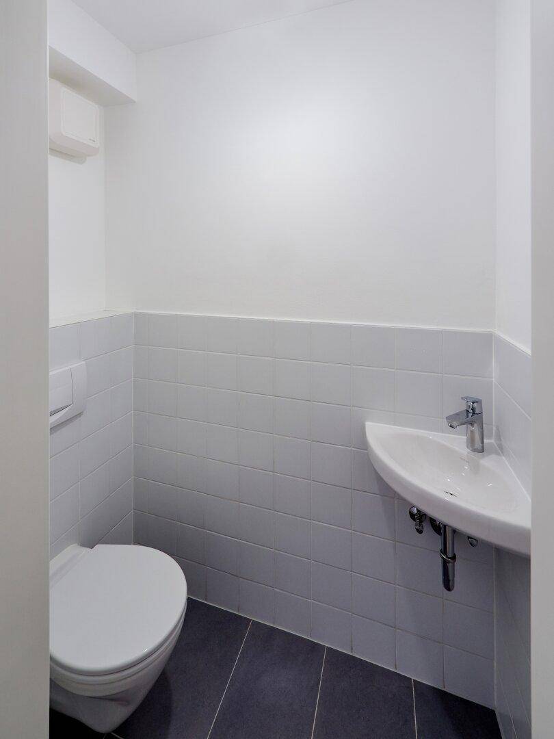 Kleines Gäste-WC mit weißen Fliesen, wandhängendem WC und einem praktischen Eckwaschbecken.