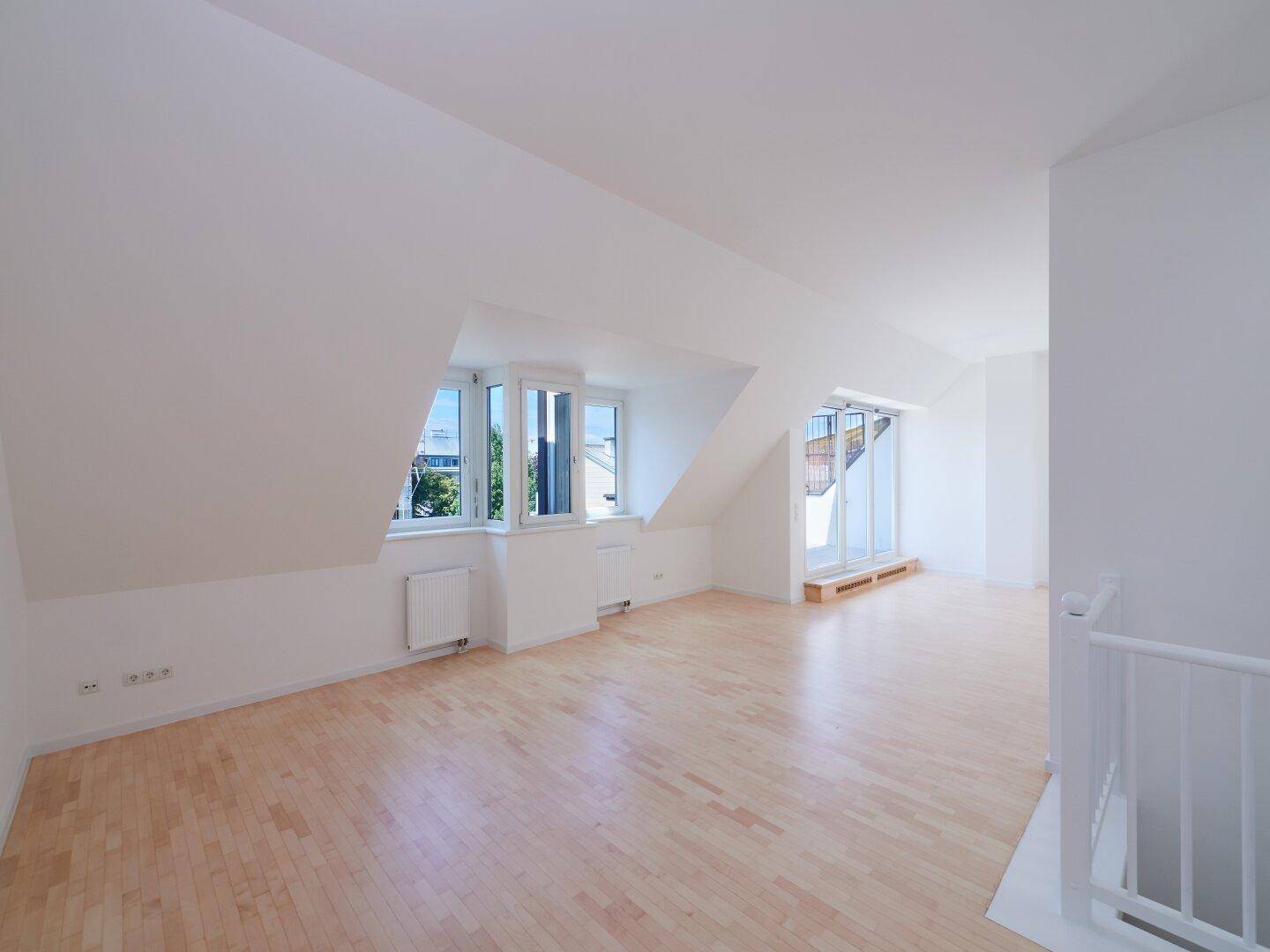 Helles Dachgeschosszimmer mit Holzboden, schrägen Wänden und mehreren Fenstern, bereit zur Einrichtung.