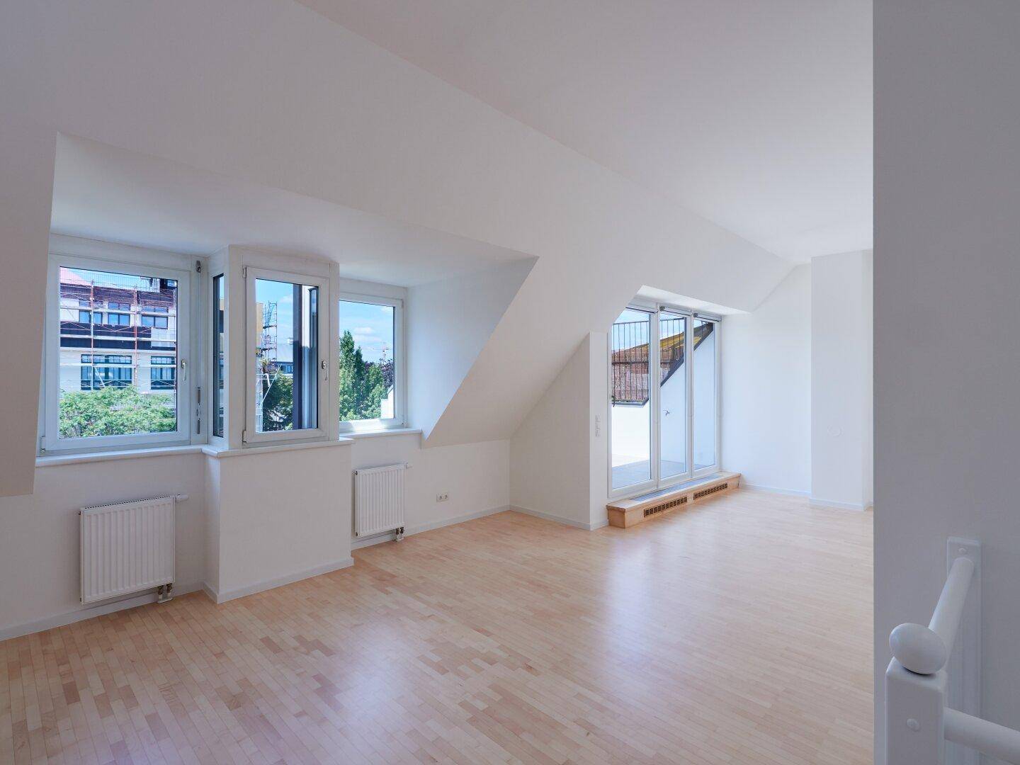 Geräumiges Dachgeschosszimmer mit Holzboden, schrägen Wänden und großen Fenstern, die viel Licht spenden.