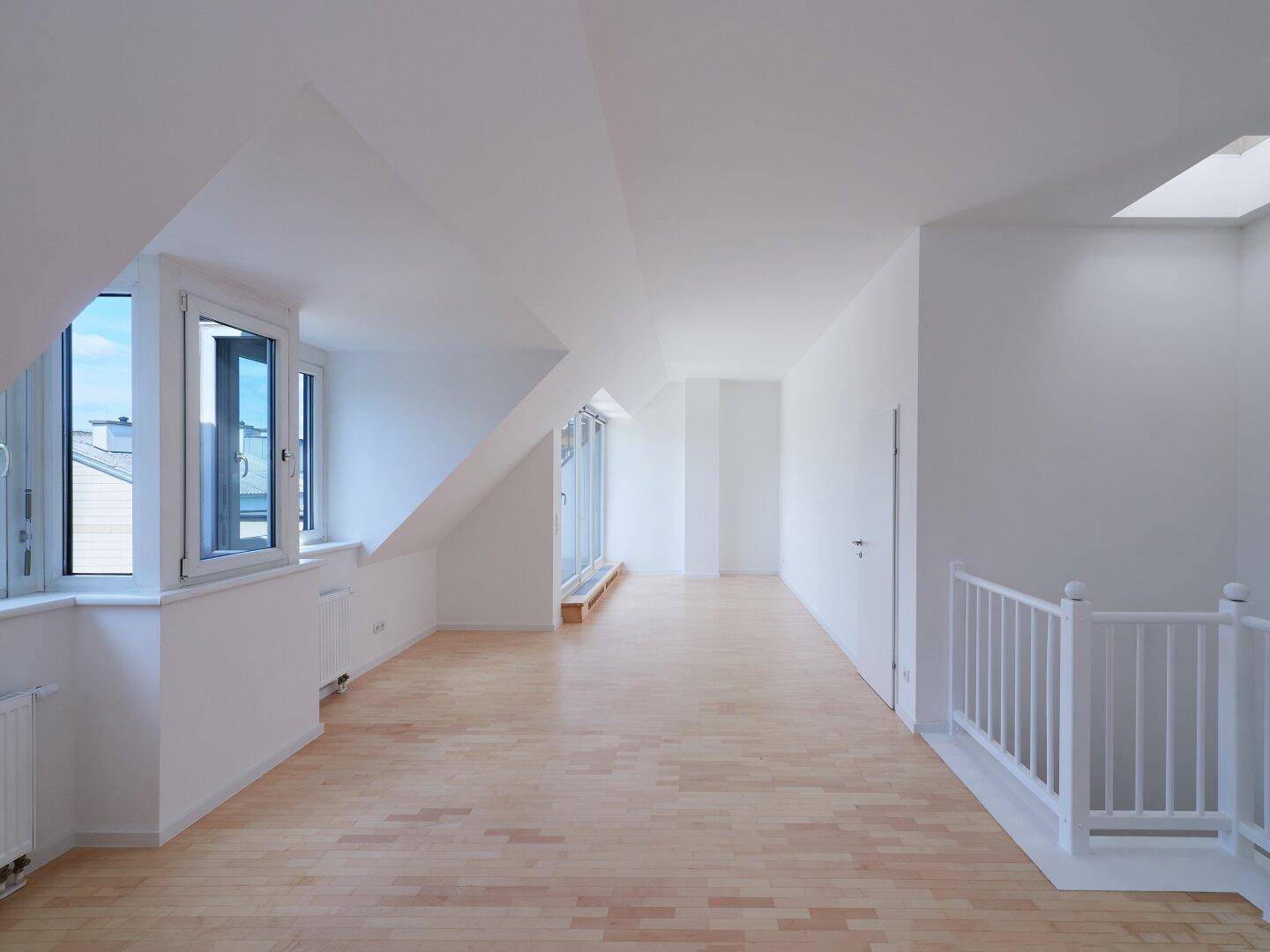 Helles Dachgeschosszimmer mit Holzboden, schrägen Wänden, großen Fenstern und einem Oberlicht.