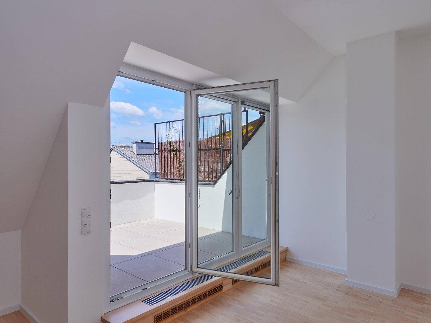 Heller Innenraum mit Zugang zu einer gefliesten Dachterrasse durch eine große Glastür.