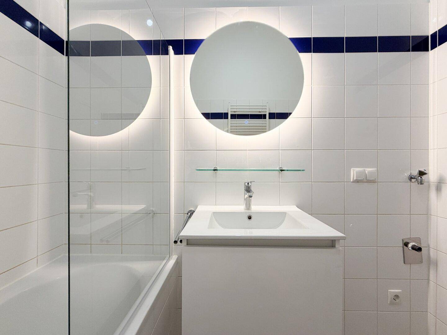 Nahaufnahme des modernen Waschtischs mit beleuchtetem Spiegel und weißer Fliesenwand im Badezimmer.