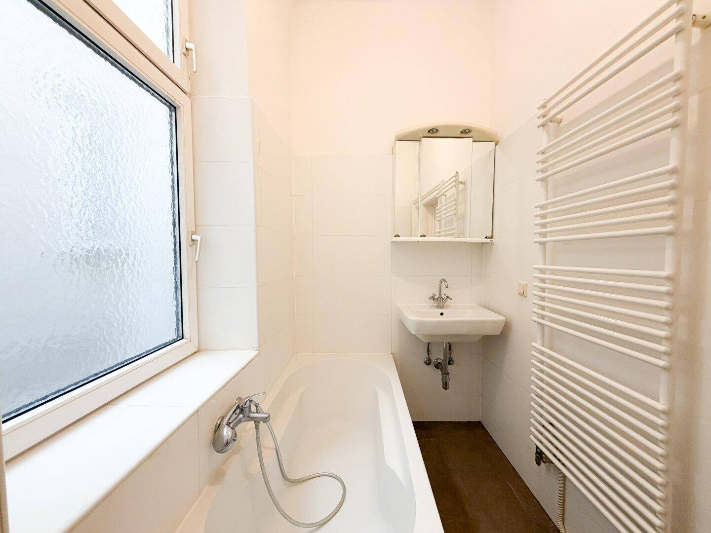 Helles Badezimmer mit Badewanne, Waschbecken, Spiegelschrank und beheiztem Handtuchhalter.