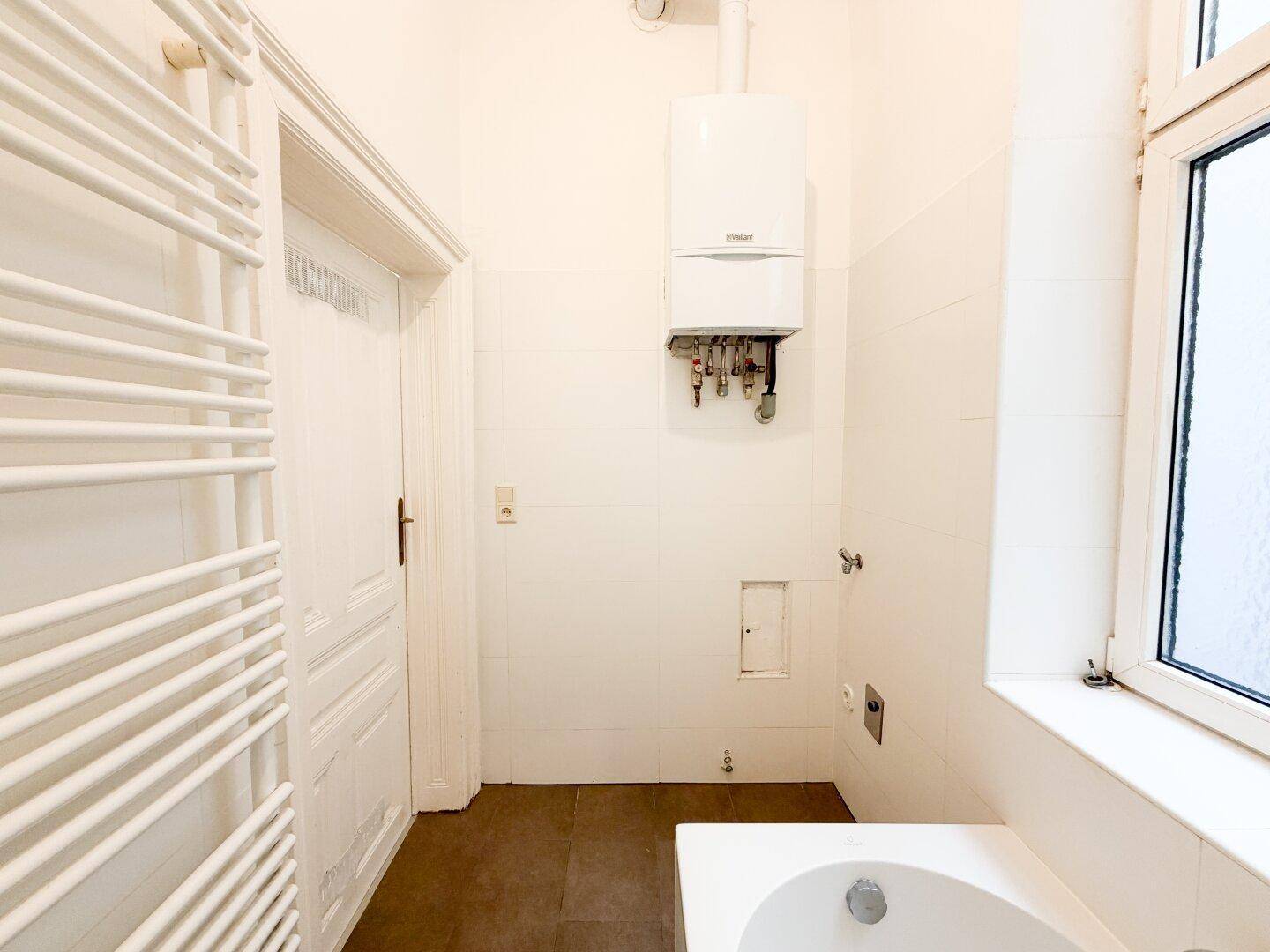 Badezimmer mit Badewanne, beheiztem Handtuchhalter und Gastherme an der Wand.
