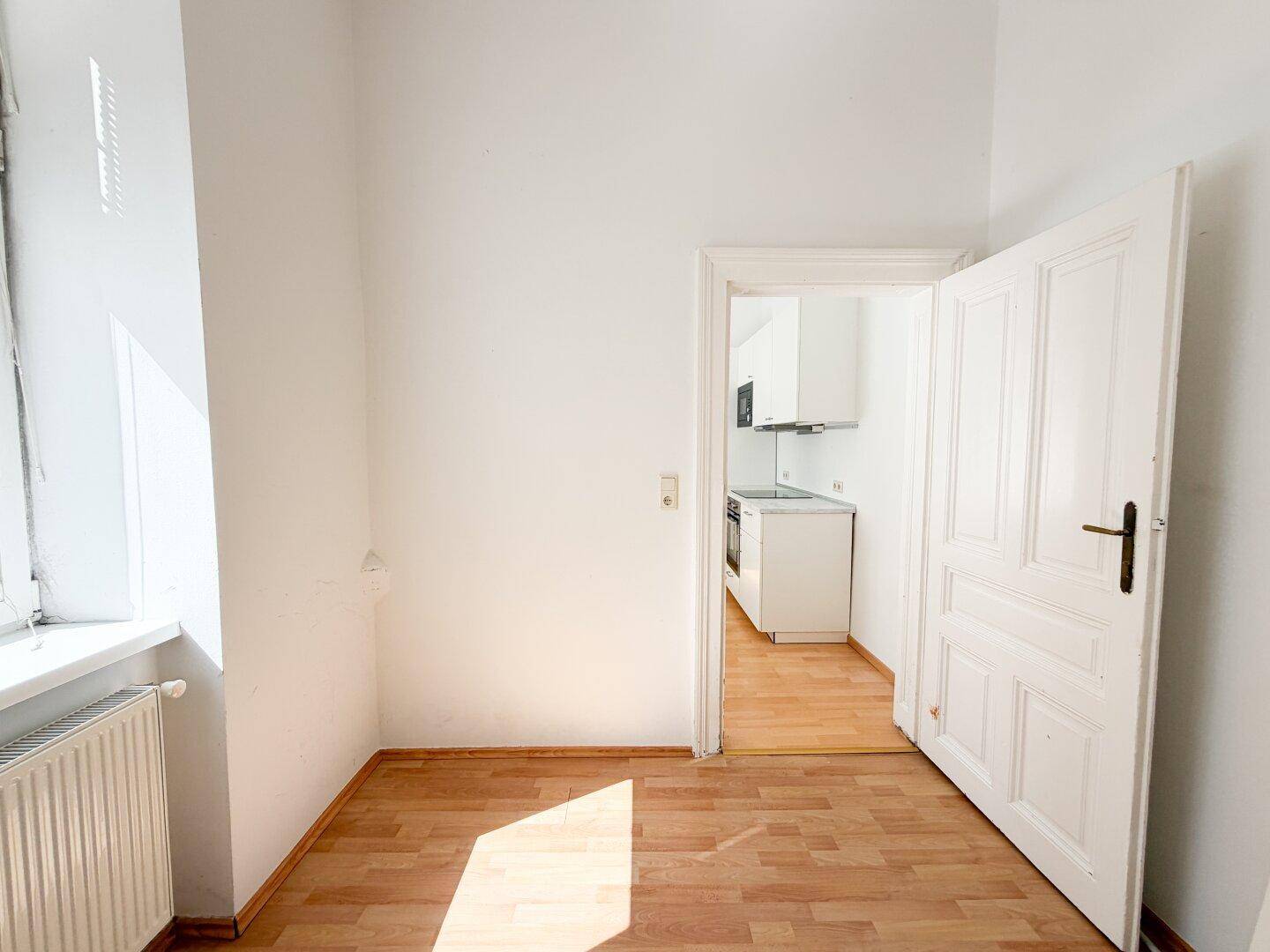 Helles Zimmer mit Laminatboden und Blick in die moderne Küche, vielseitig nutzbar.