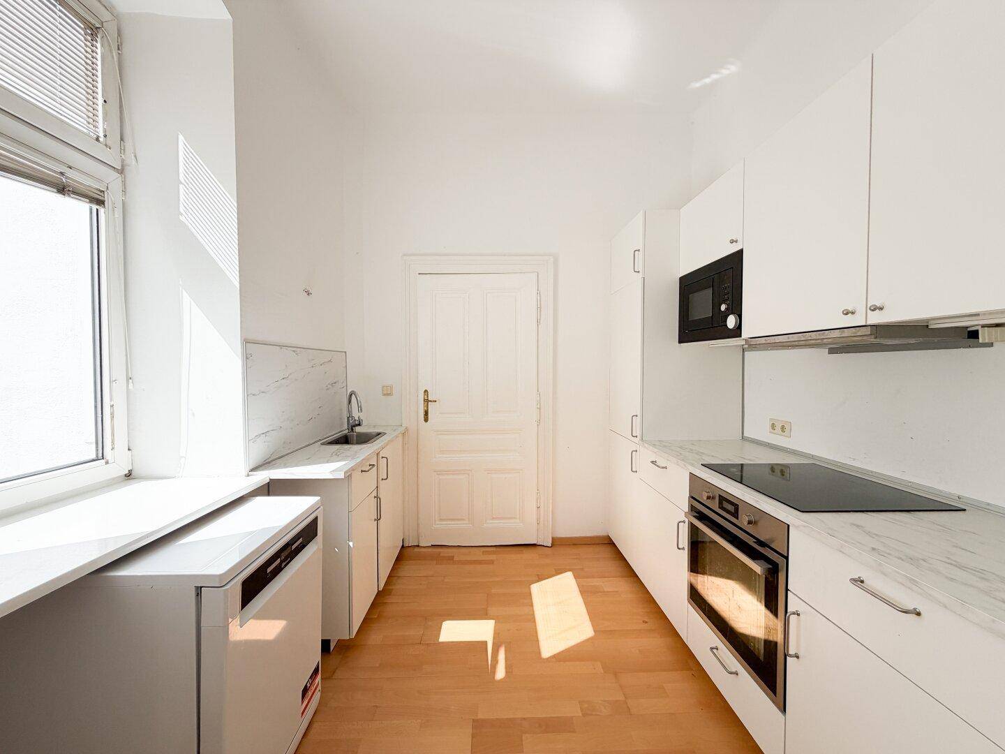 Moderne weiße Küche mit Einbaugeräten, Induktionskochfeld und hellem Laminatboden.