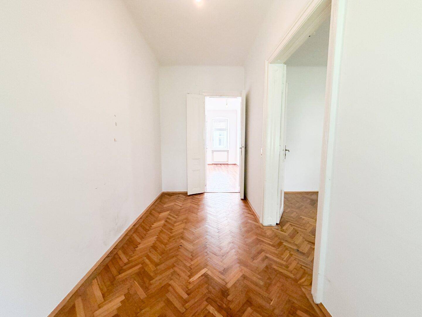 Langer Flur mit Fischgrätparkett und hohen Türen, verbindet die einzelnen Räume der Wohnung.