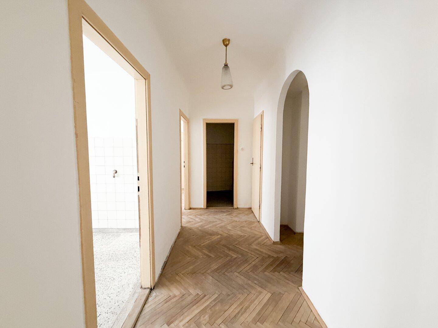 Langer Flur mit Fischgrätparkettboden und mehreren Türen, verbindet verschiedene Räume der Wohnung.