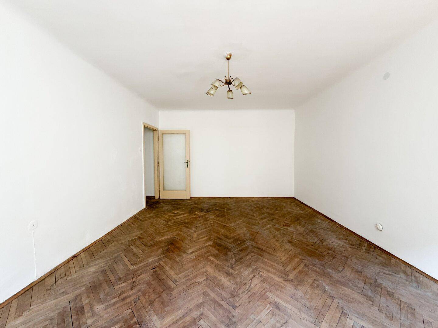 Geräumiges Zimmer mit klassischem Fischgrätparkett und einer Holztür, ideal für Wohn- oder Schlafbereich.