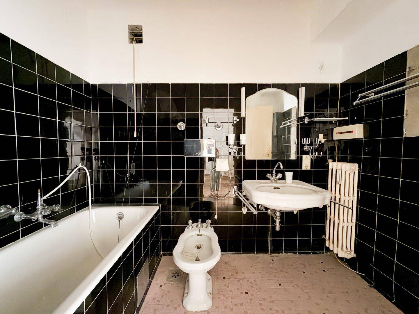 Badezimmer mit schwarzen Fliesen, Badewanne, Bidet und einem Waschbecken im klassischen Stil.