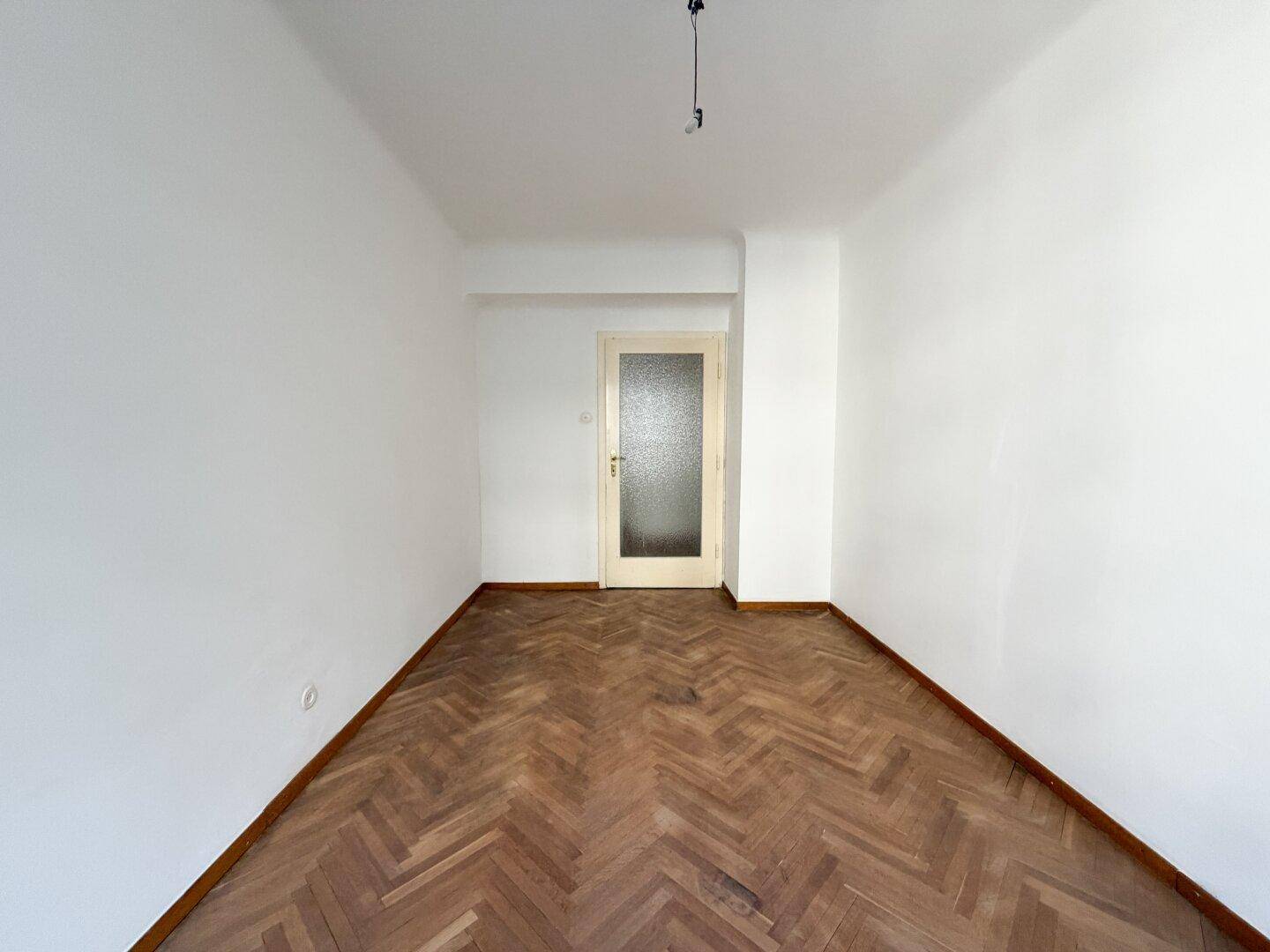 Schlichtes Zimmer mit Fischgrätparkett und einer Tür mit Milchglas, bereit zur Einrichtung.