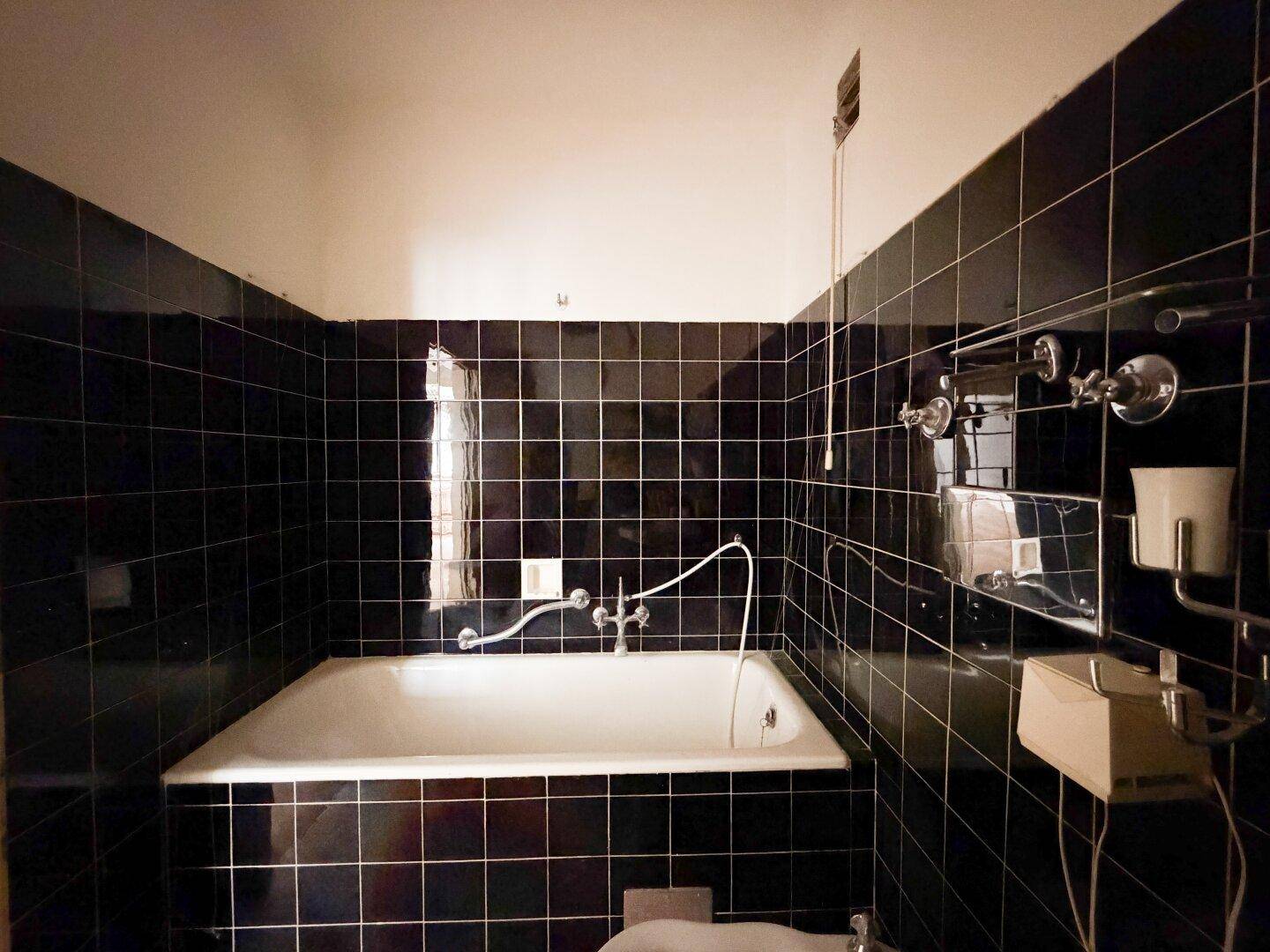 Badezimmer mit schwarzen Fliesen, einer Badewanne und einem kleinen Fenster.