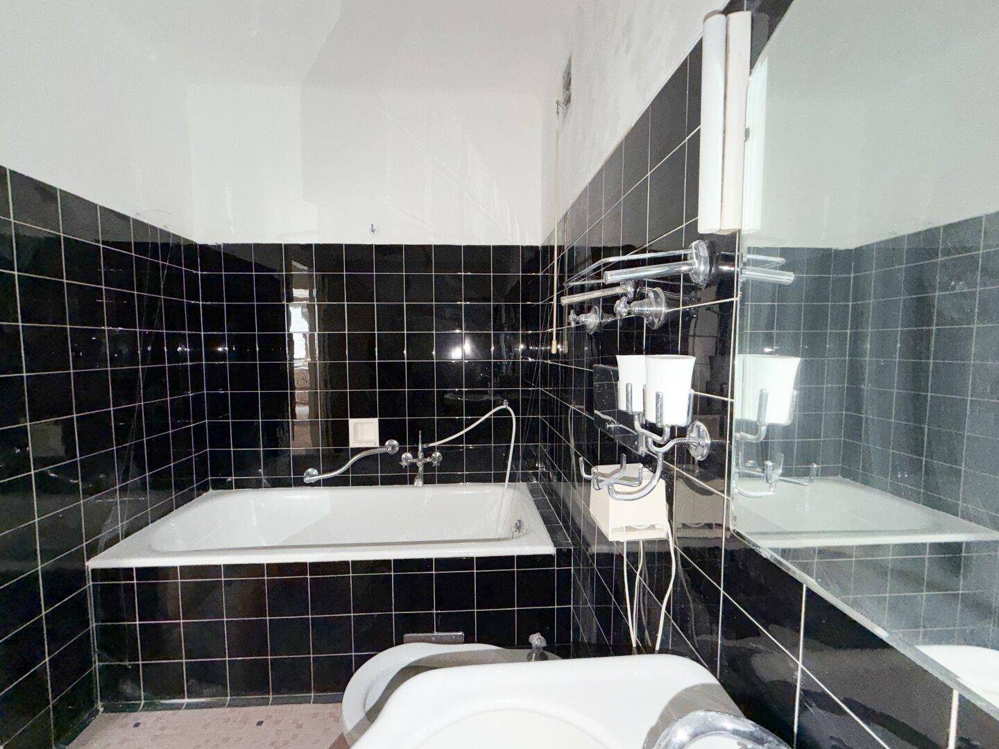 Badezimmer mit schwarzen Fliesen, Badewanne und einem Spiegel über dem Waschtisch.