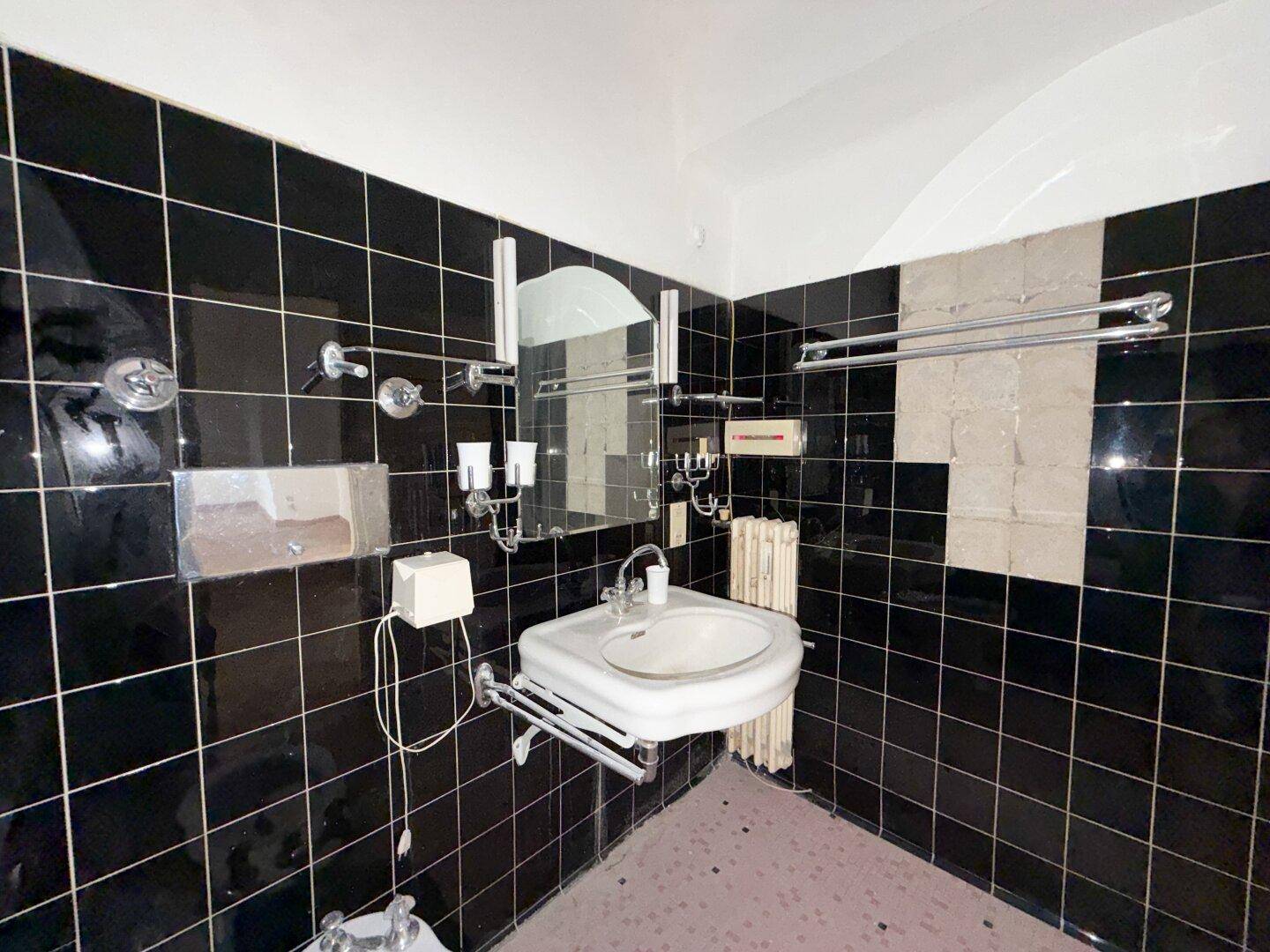 Badezimmer mit schwarzen Fliesen, Waschbecken und einem Spiegel über dem Waschtisch.